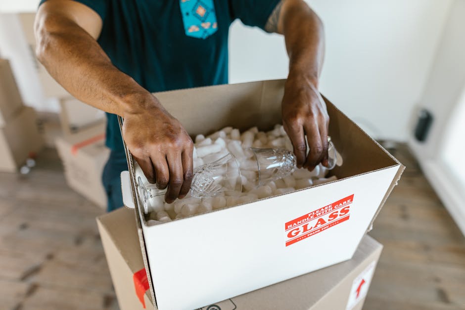 Hands carefully packing glassware with protective padding into a moving box