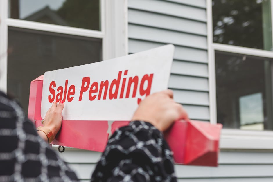 Close-up of hands holding a sale pending sign in front of a home