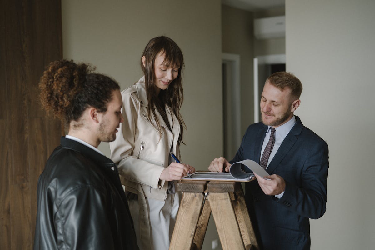 A couple signing real estate documents with a realtor inside a new apartment