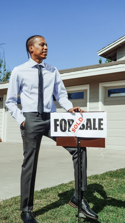Realtor beside sold sign in front of home