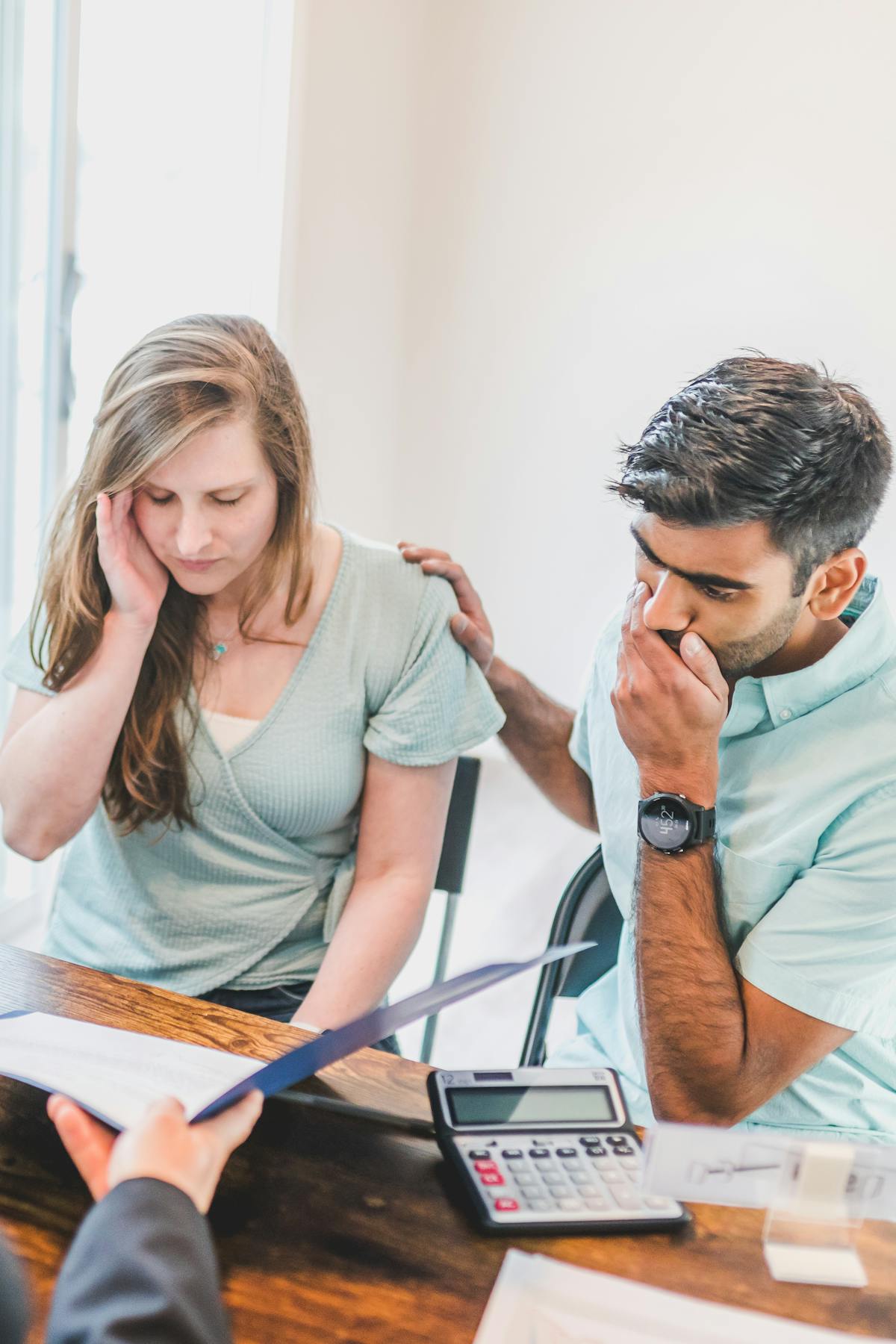 A young couple sitting with a real estate agent reviewing contingency documents and looking concerned about home buying conditions