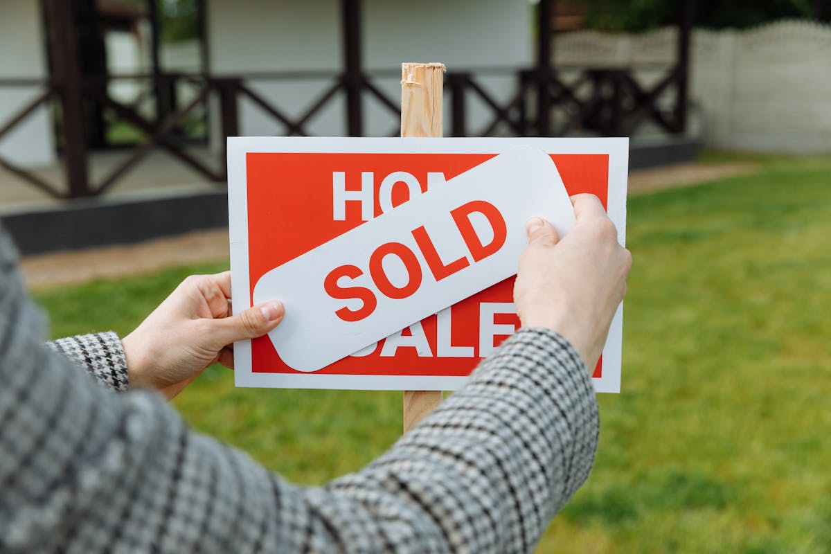 Hands placing a sold sticker on a real estate sign after all contingencies were met and the home sale closed